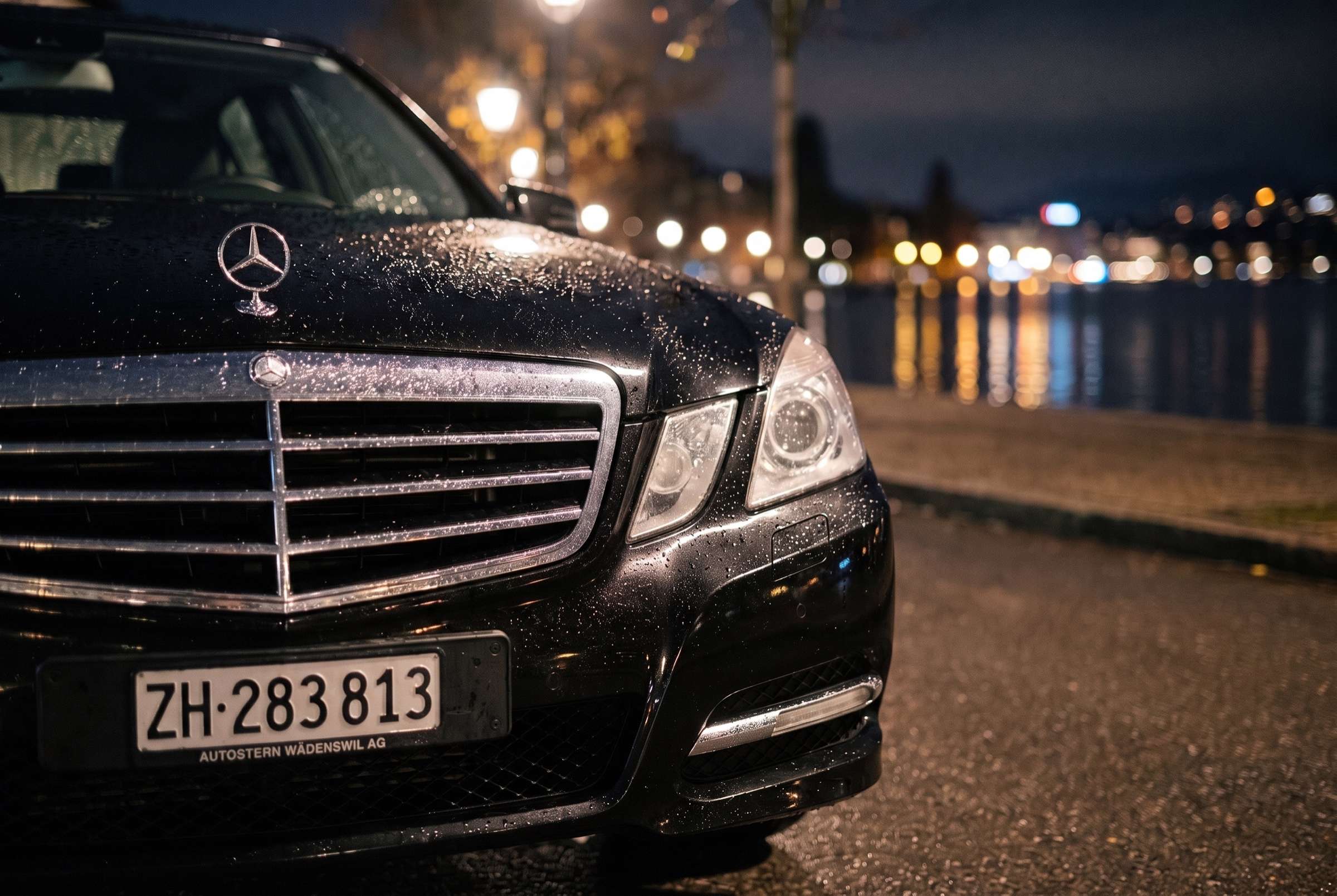 Kühlergrill und Scheinwerfer der schwarzen Mercedes E-Klasse nach dem Regen, nachts am See